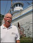 Chuck Epifanio next to the decaying fishing boat was once the Flagship Restaurant. Credit: Michael W. Fincham